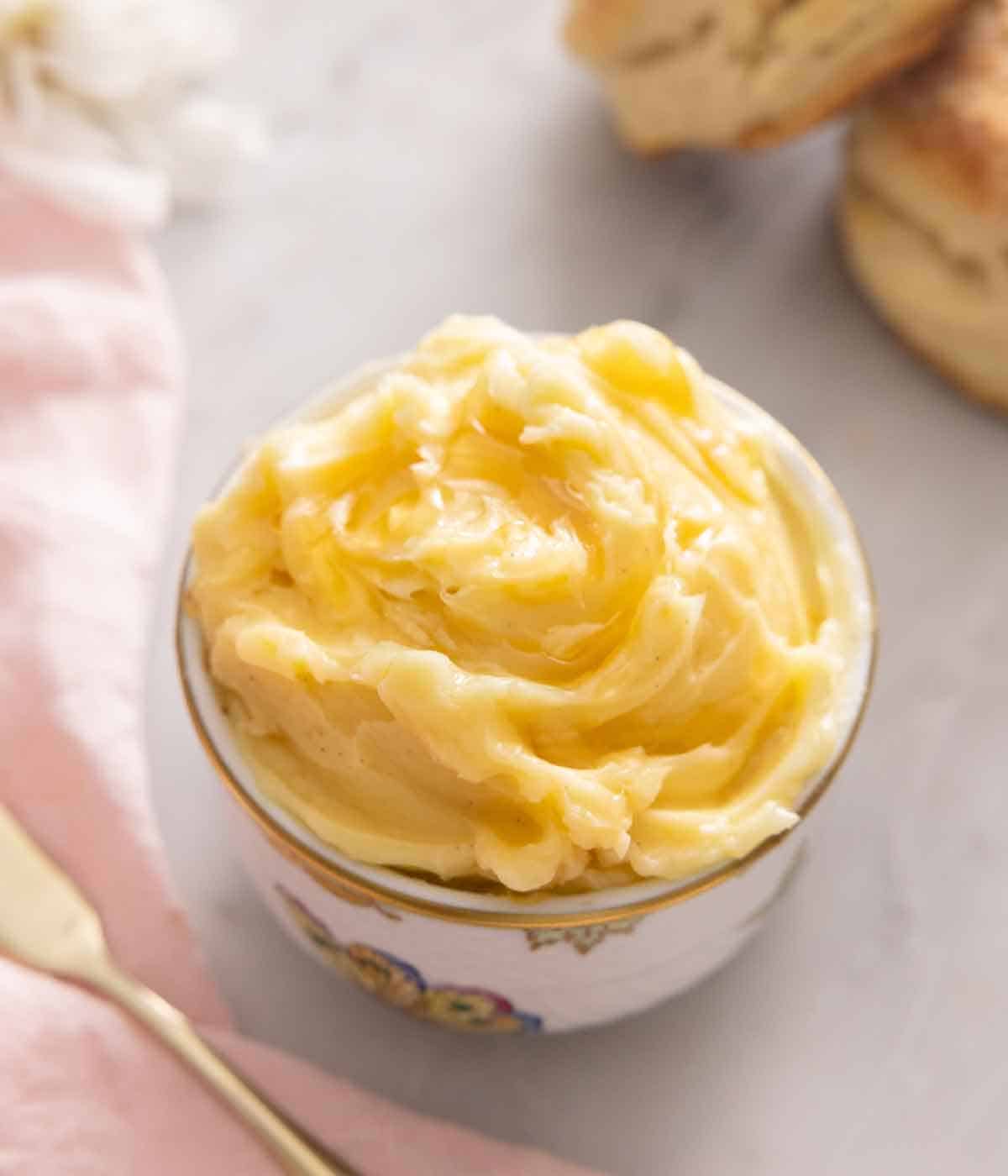 A bowl of honey butter beside a linen napkin and biscuits in the background.