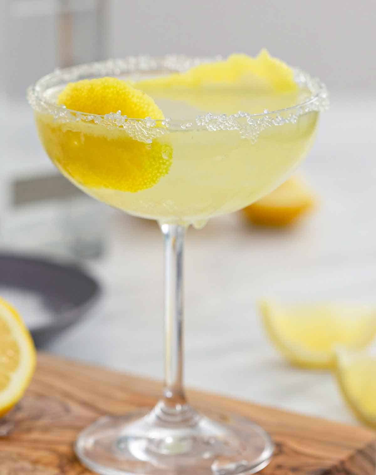 A lemon drop martini with sugar on the rim and lemon peel in the glass on a wooden cutting board.