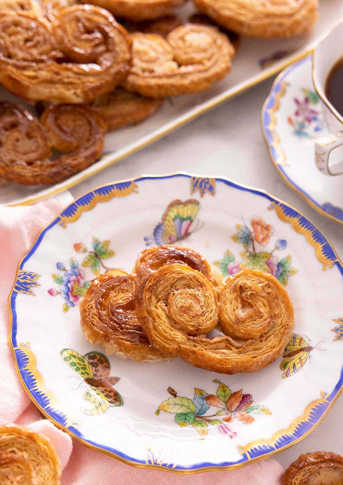 A plate with two palmiers in front of a platter with more.