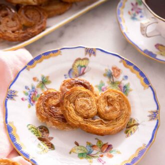 Pinterest graphic of a plate of two palmiers by a cup of coffee and a platter of more palmiers.