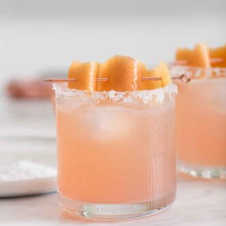 Pinterest graphic of a glass of paloma with a citrus peel for garnish.