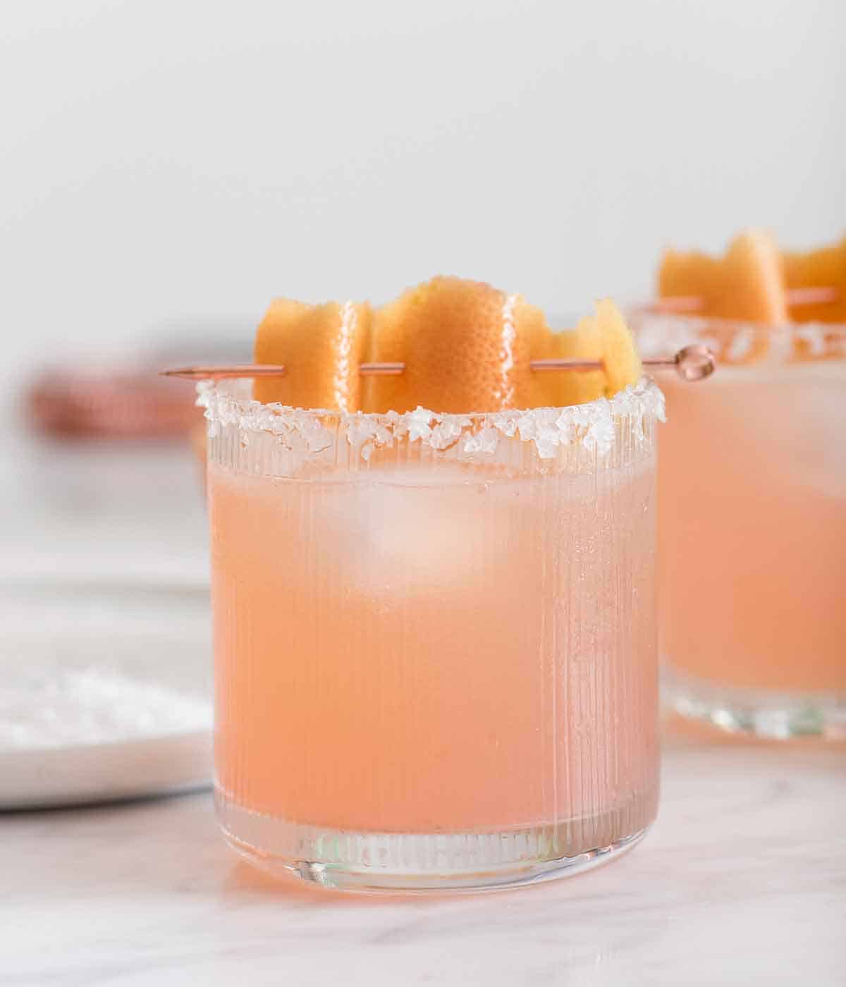A glass of paloma with a salted rim with a grapefruit peel garnish on top.
