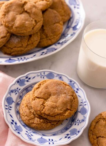 A plate with two pumpkin snickerdoodles with a larger plate containing more behind it with a glass of milk.