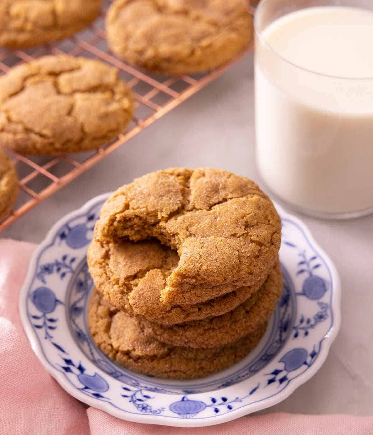 A plate with a stack of pumpkin snickerdoodles with one cookie missing a bite, beside a glass of milk.