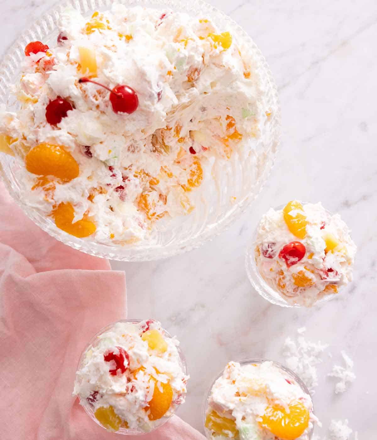 Overhead view of a bowl of ambrosia salad with three servings scooped out into cups beside it.