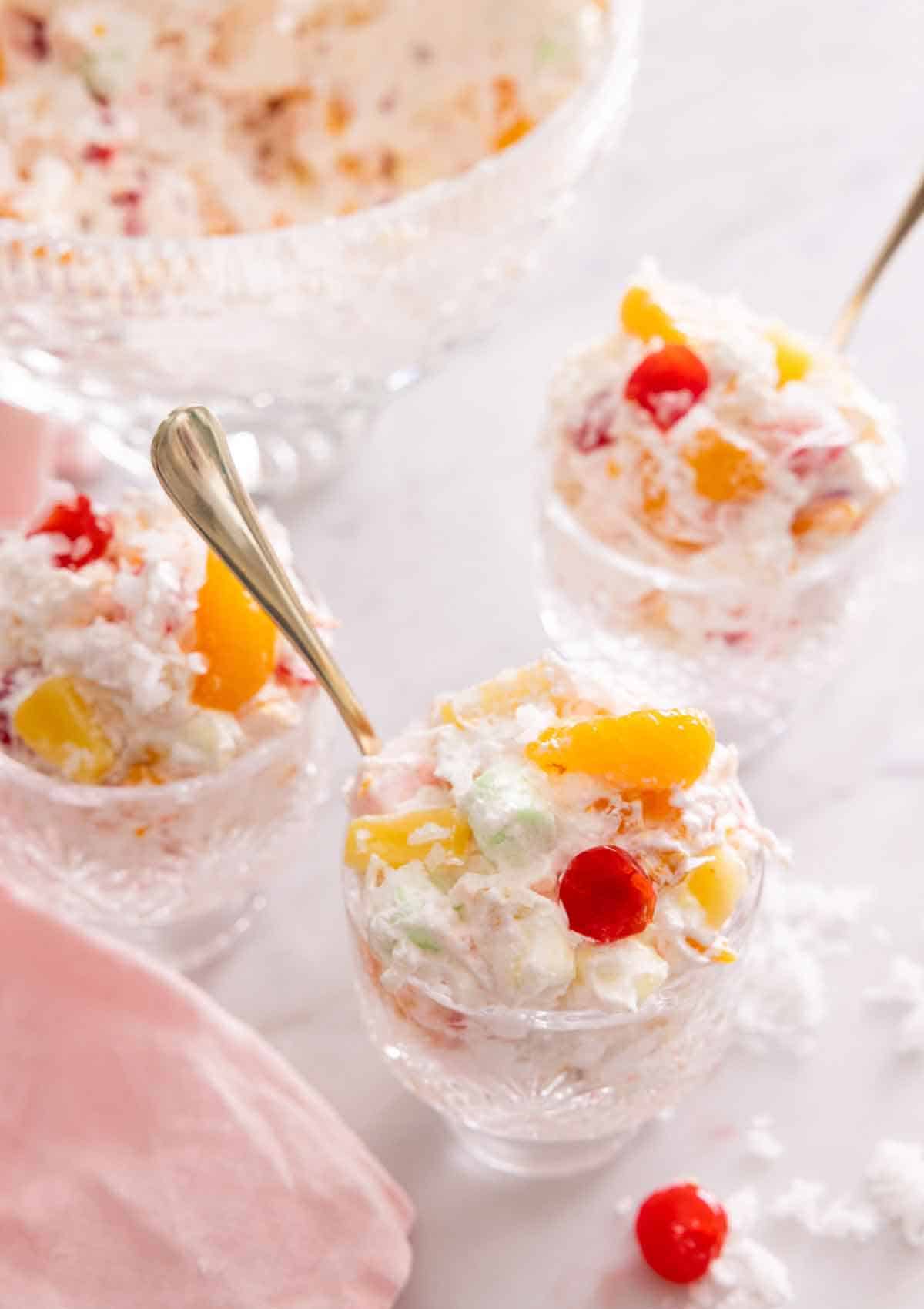 Three cups of ambrosia salad with spoons inserted beside a pink linen napkin.
