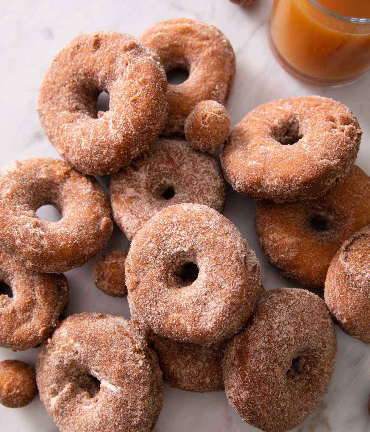 Multiple apple cider donuts piled on top of each other on a marble countertop.