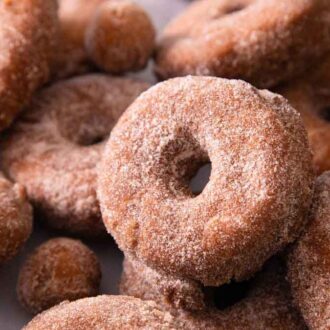 Multiple apple cider donuts and donut holes with one in focus in the middle.