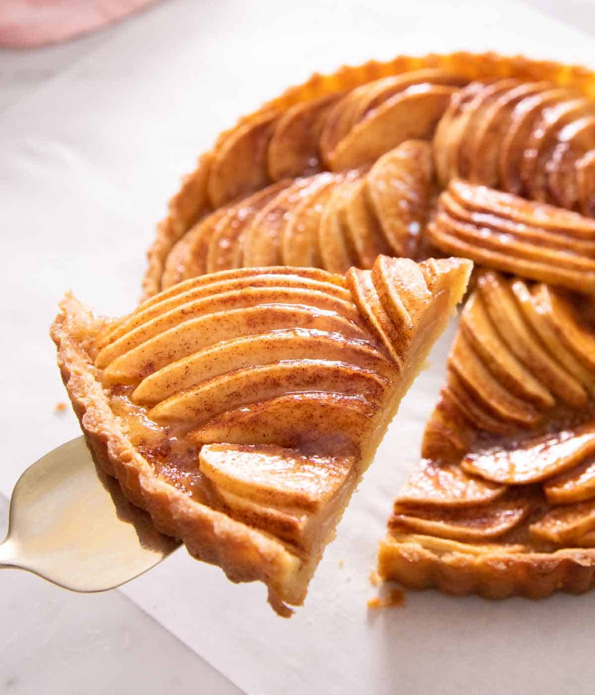 A slice of apple tart being lifted up from the tart.