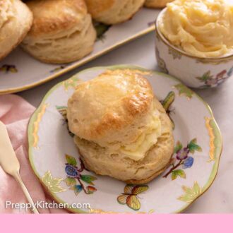 Pinterest graphic of a biscuit cut in half with butter spread on it with more biscuits in the back and a bowl of butter.