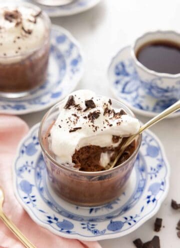 A glass of chocolate mousse with whipped cream and shaved chocolate with a spoonful eaten and a spoon inside.