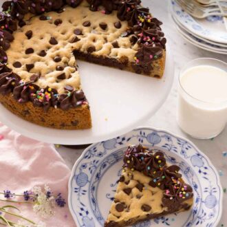 Pinterest graphic of a cookie cake on a cake stand with a slice cut and served on a plate in front.