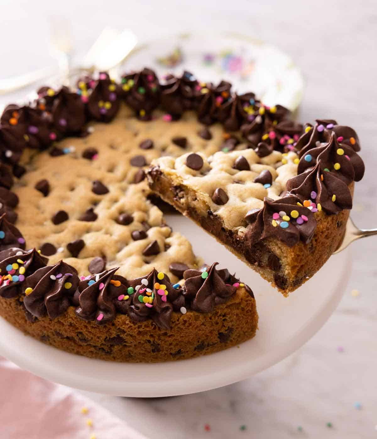 A slice of cookie cake lifted out of the rest of the cake on a cake stand.