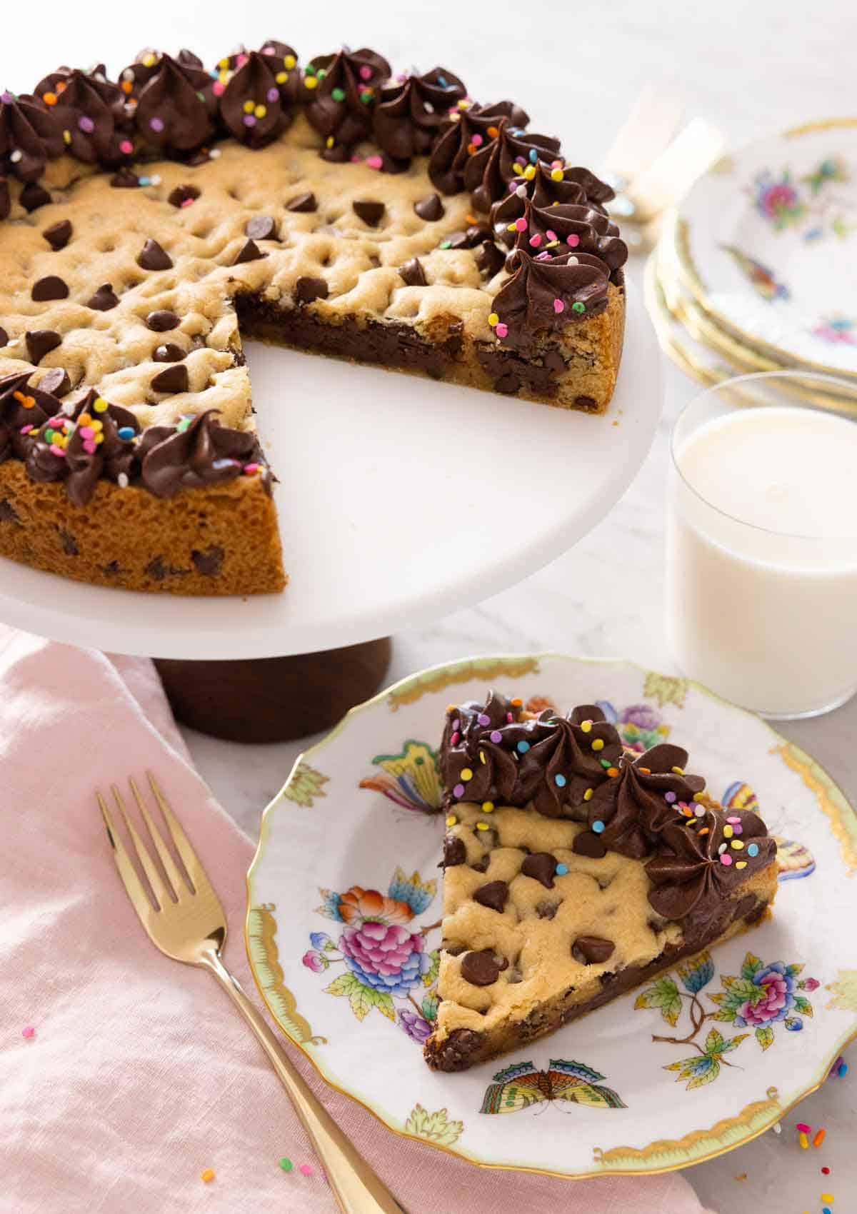A cake stand with a cookie cake with a slice removed and placed on a plate.