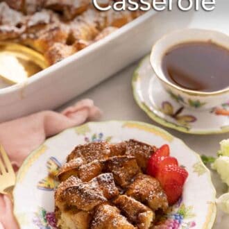 Pinterest graphic of a plate with a serving of French toast casserole with sliced strawberries in front of a cup of coffee.