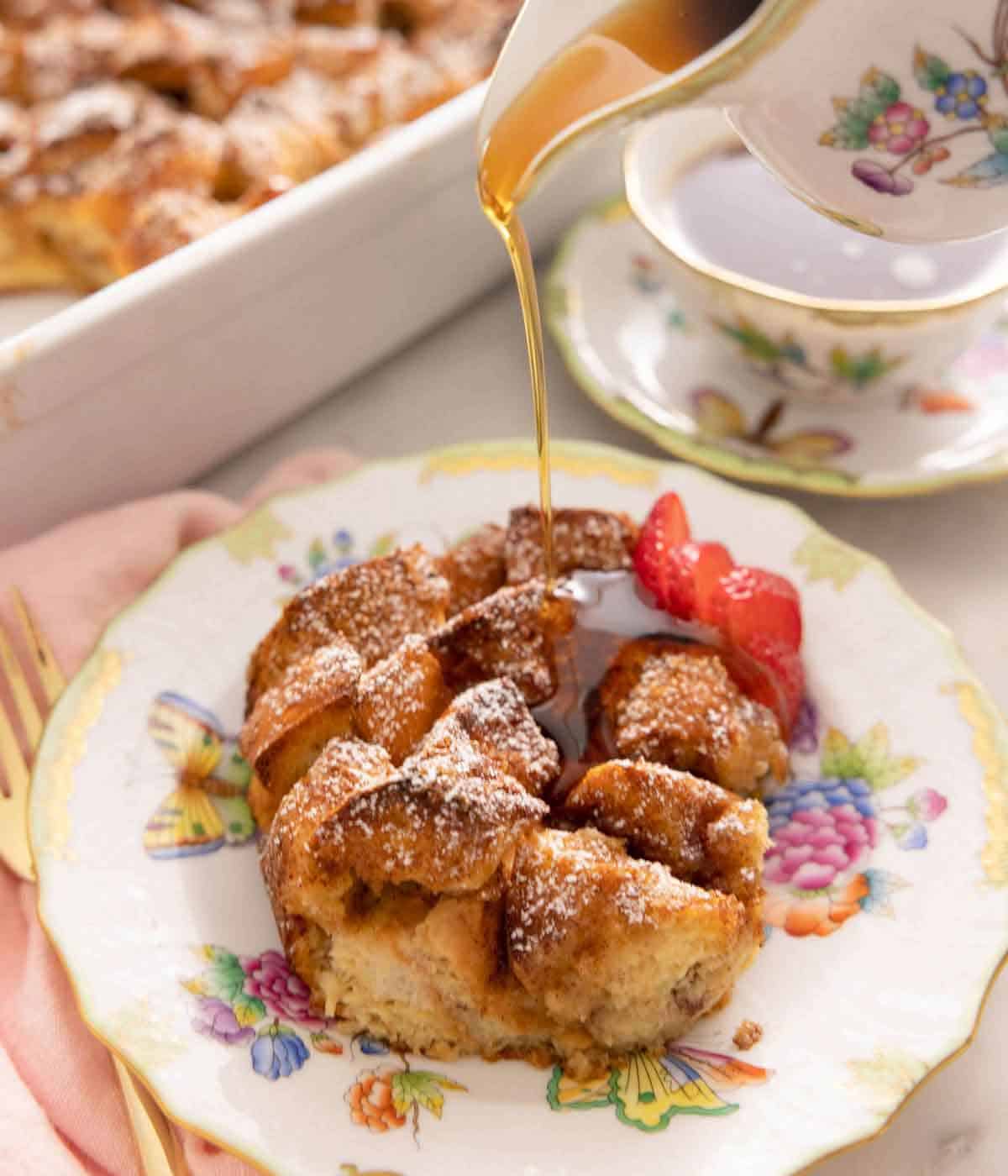 A serving of French toast casserole with sliced strawberries on a plate with maple syrup drizzled on top.