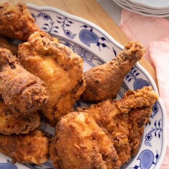 Pinterest graphic of a platter of fried chicken on a wooden board beside a pink linen napkin.