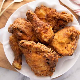Overhead view of a plate with fried chicken on a serving board beside a linen napkin.