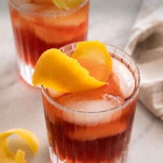 Pinterest graphic of an angled overhead view of three glasses of Negroni with ice and orange peel garnish on top.