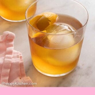 Pinterest graphic a glass of old fashioned with a sphere ice cube and orange peel inside.