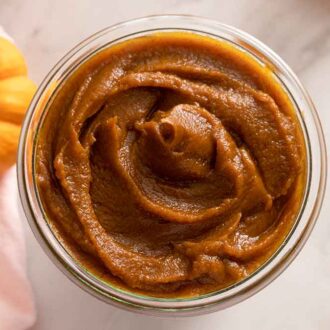 Overhead view of a jar of pumpkin butter beside a tiny decorative pumpkin.