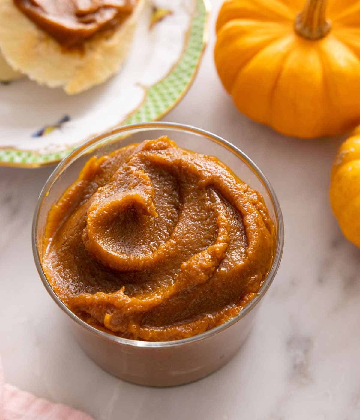 A glass jar of pumpkin butter with mini pumpkins in the background.