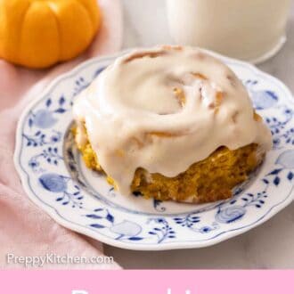 A plate with a pumpkin cinnamon roll with cream cheese on top.