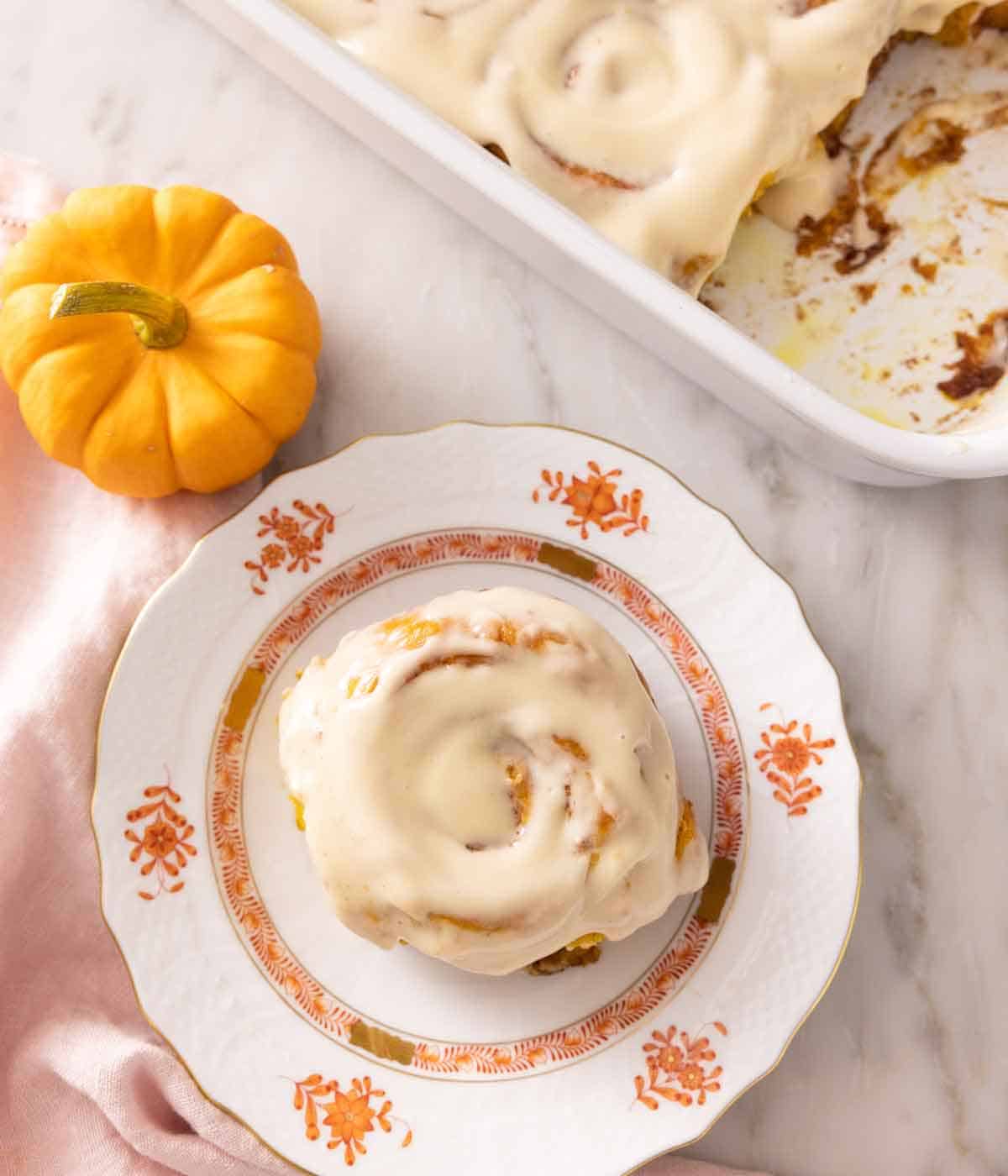 Overhead view of a plate with a pumpkin cinnamon roll with cream cheese frosting.