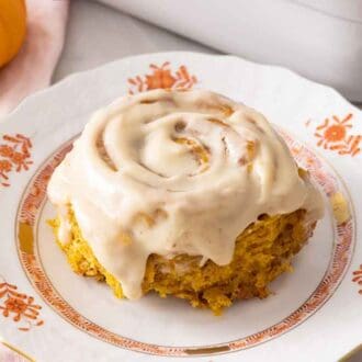 A plate with pumpkin cinnamon roll with cream cheese frosting on top.