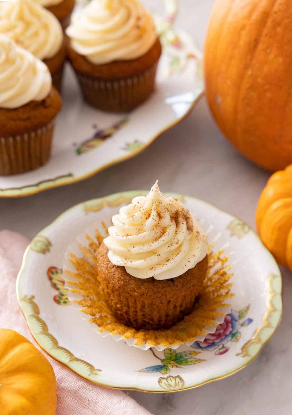 A plate with a pumpkin cupcake with cream cheese frosting on top with the cupcake liner pulled away.