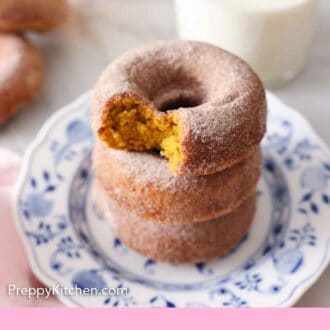 Pinterest graphic of a plate of three stacked pumpkin donuts with a cinnamon sugar coating. The top one has a bite taken out of it.