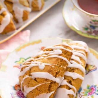 Pinterest graphic of two pumpkin scones on a plate in front of a cup of tea and more scones.