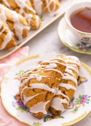A plate with two pumpkin scones in front of a cup of tea and platter.