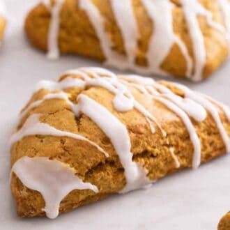 Many pumpkin scones on a marble counter with one in focus, in the middle.
