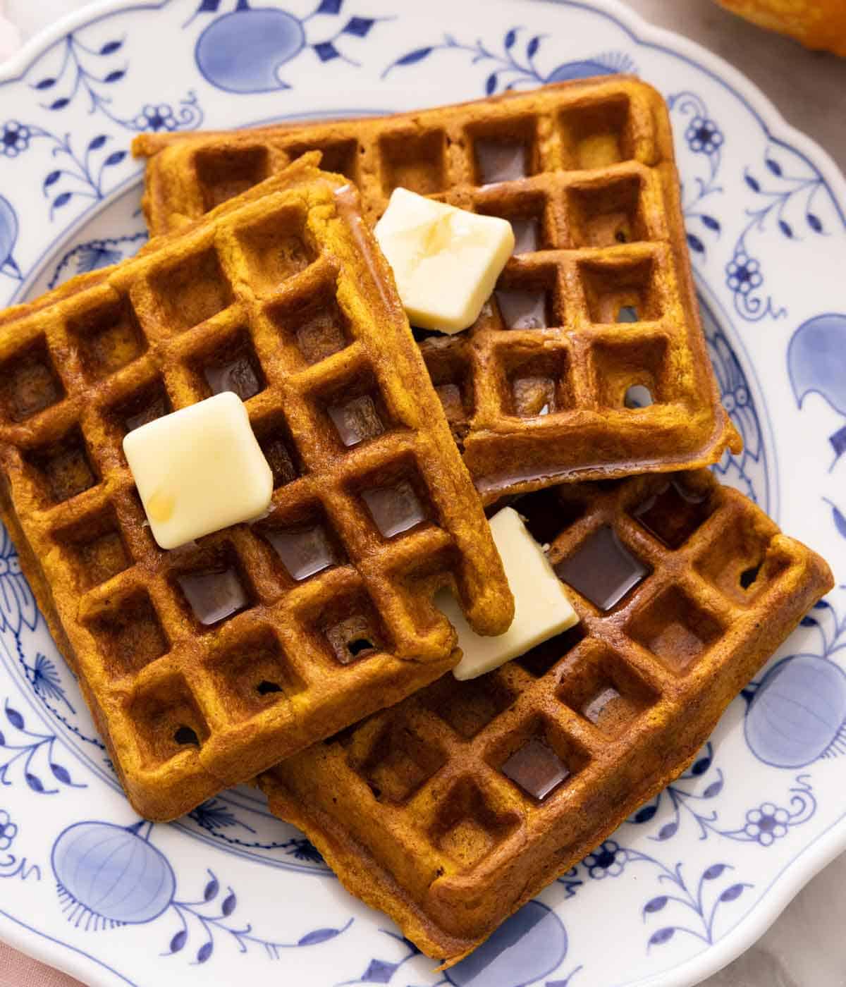 Overhead view of three pumpkin waffles with a knob of butter on top of each waffle.