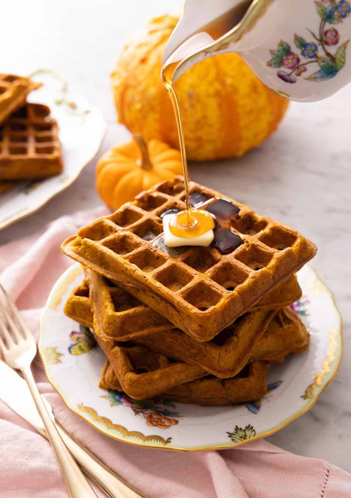 A plate with a stack of five pumpkin waffles with syrup poured on top.