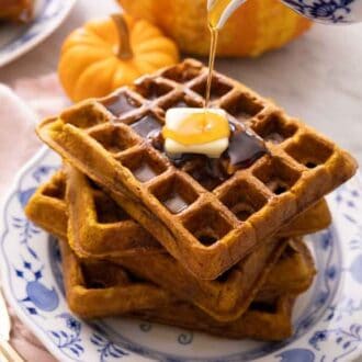 A stack of five pumpkin waffles with a piece of butter on top with syrup being poured on top.