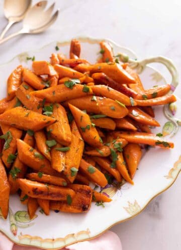 A platter of roasted carrots with parsley on top.