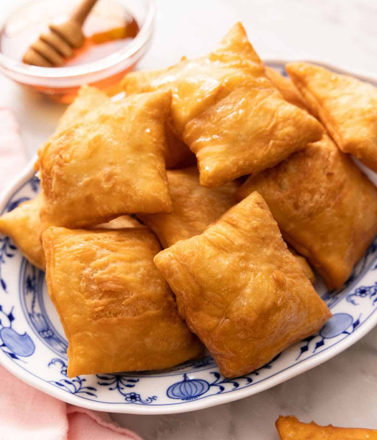 A platter of sopapillas with a bowl of honey in the back.