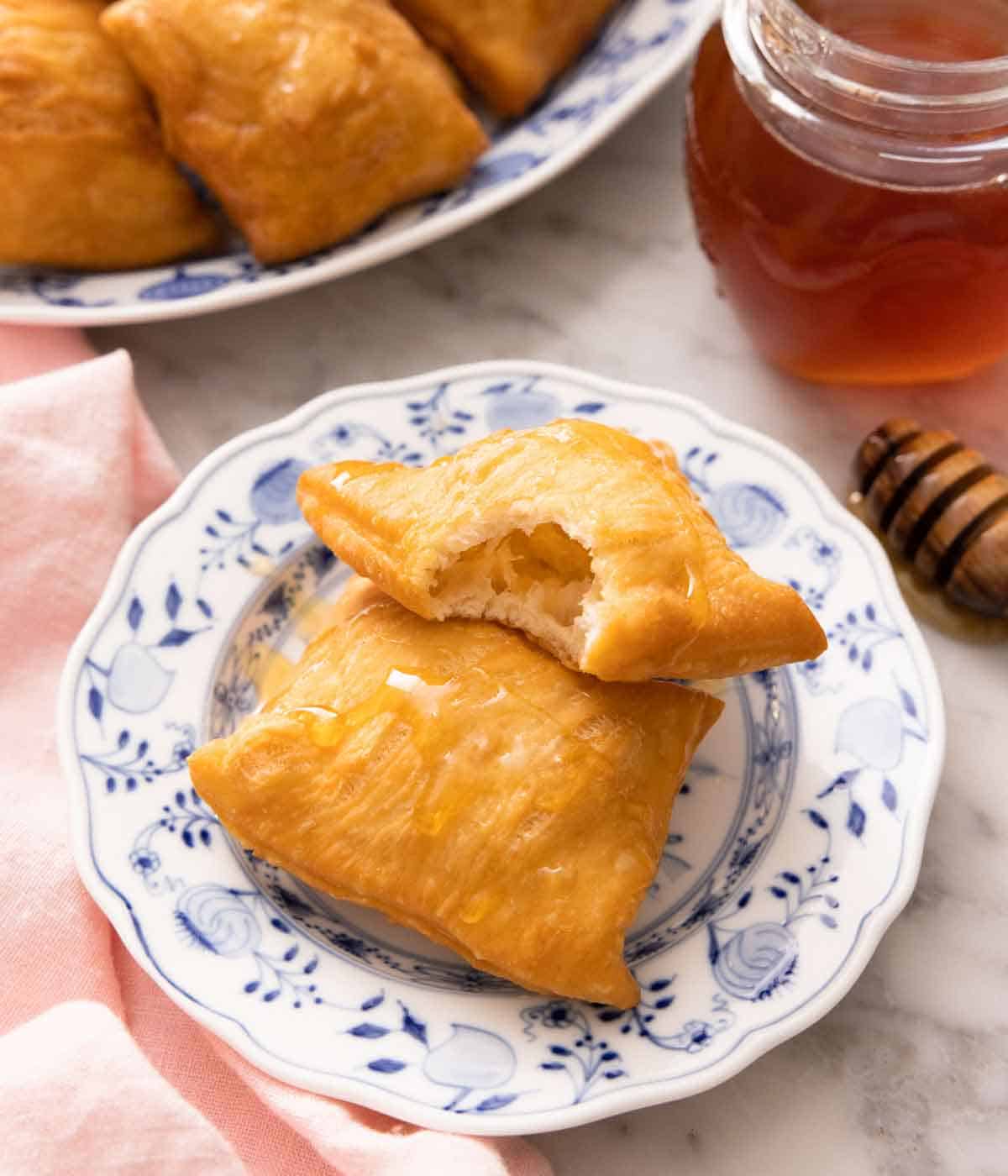 A plate with two sopapillas, one with a bite taken out of it. A jar of honey and more sopapillas in the back.