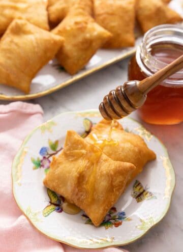 A plate with two sopapillas with honey drizzled over them.