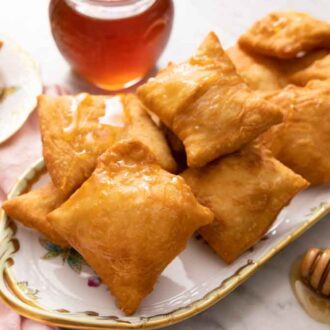 A platter with sopapillas with a honey dipper in front of it and a jar of honey in the back.