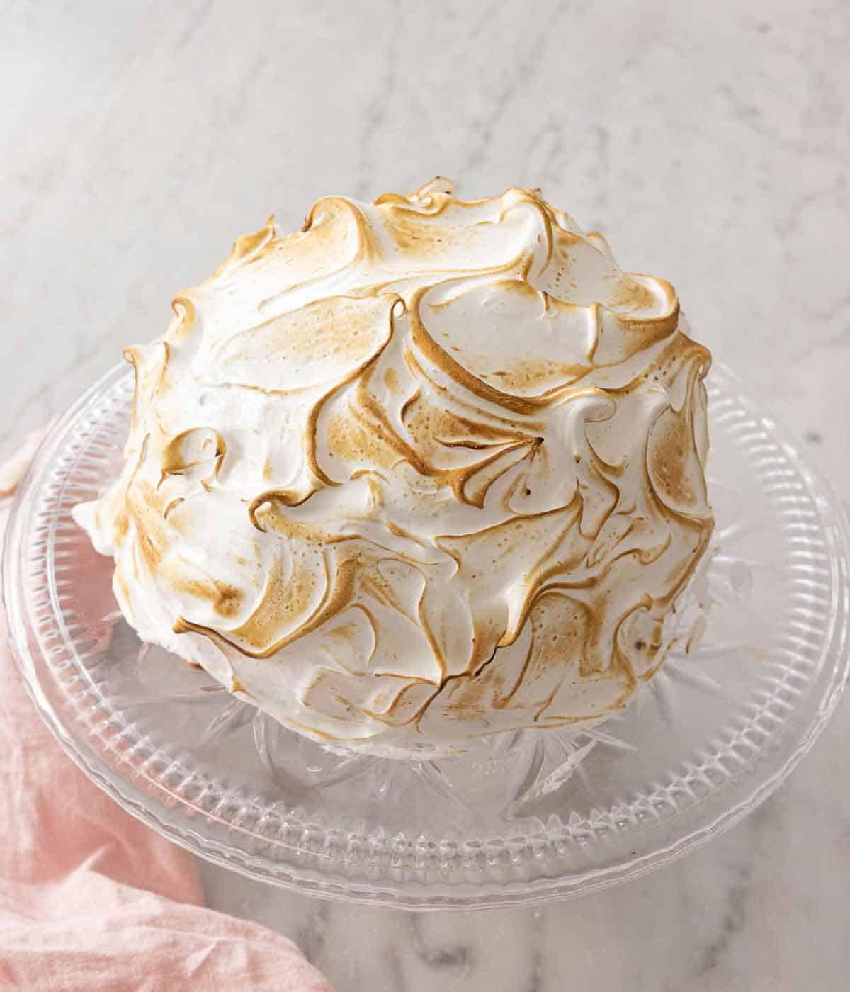 A baked Alaska on a clear cake stand.