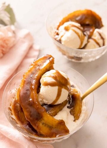 Two bowls of Banana Fosters, one in front has a spoon in it.