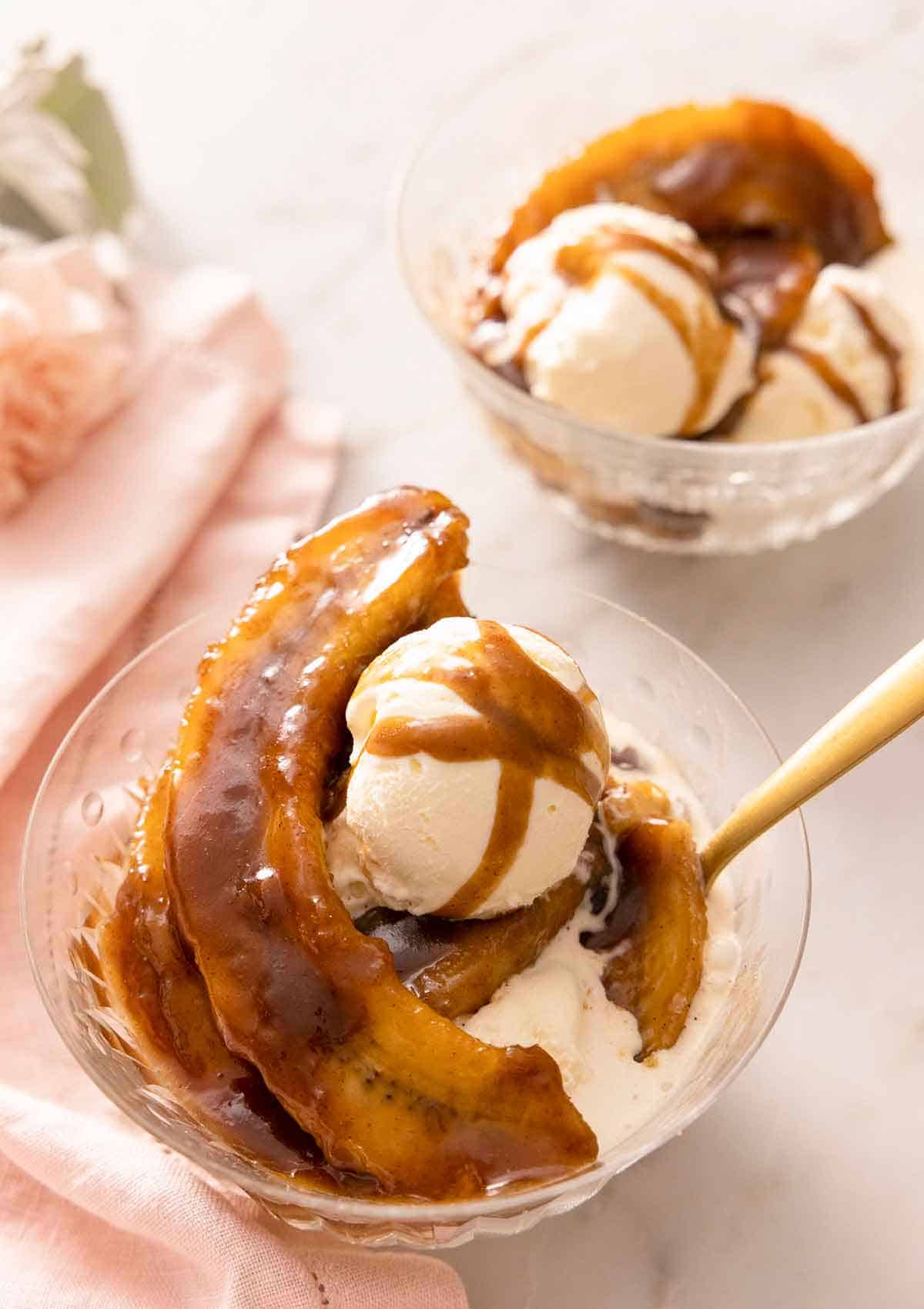 Two bowls of Banana Fosters, one in front has a spoon in it.