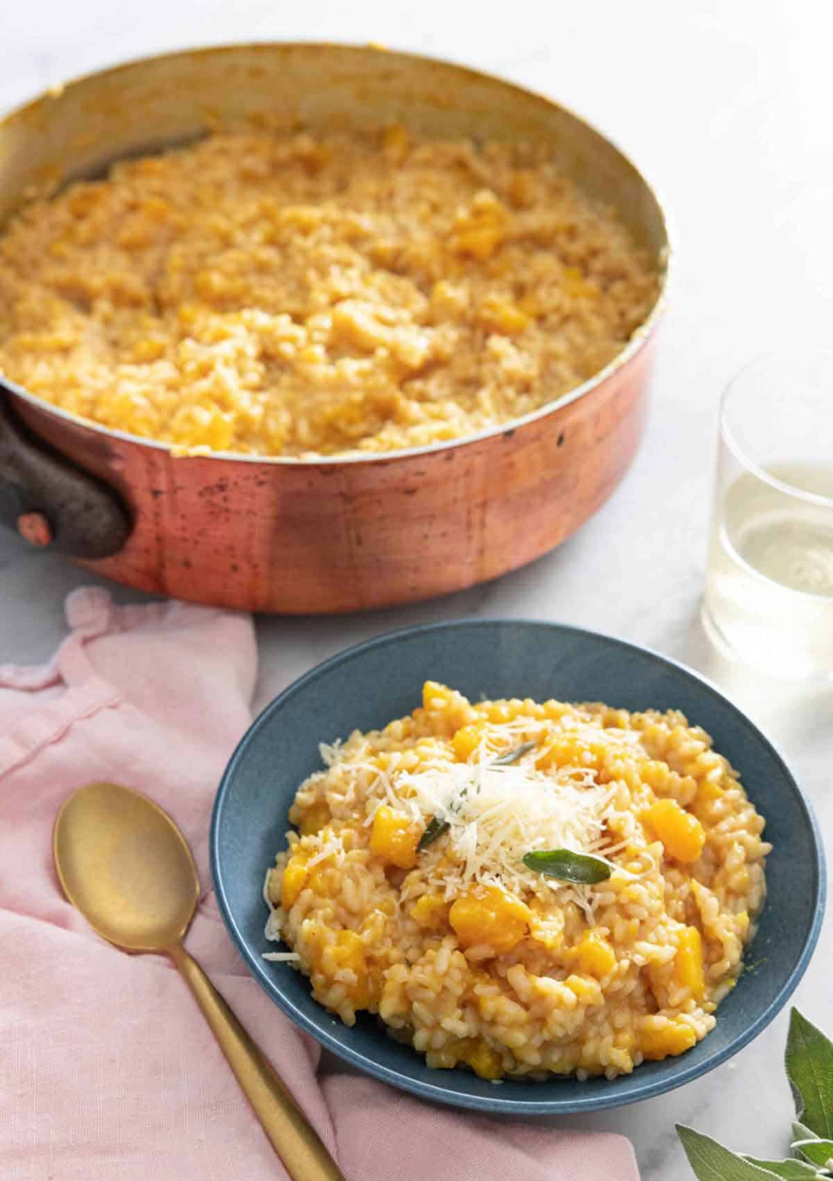 A bowl of butternut squash risotto in front of a pot with the rest.