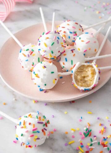 A plate with multiple cake pops on it with one with a bite taken out.