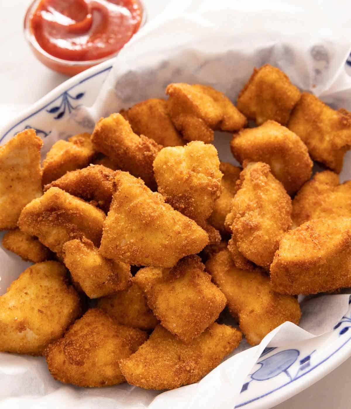 A platter of chicken nuggets with ketchup in the background.