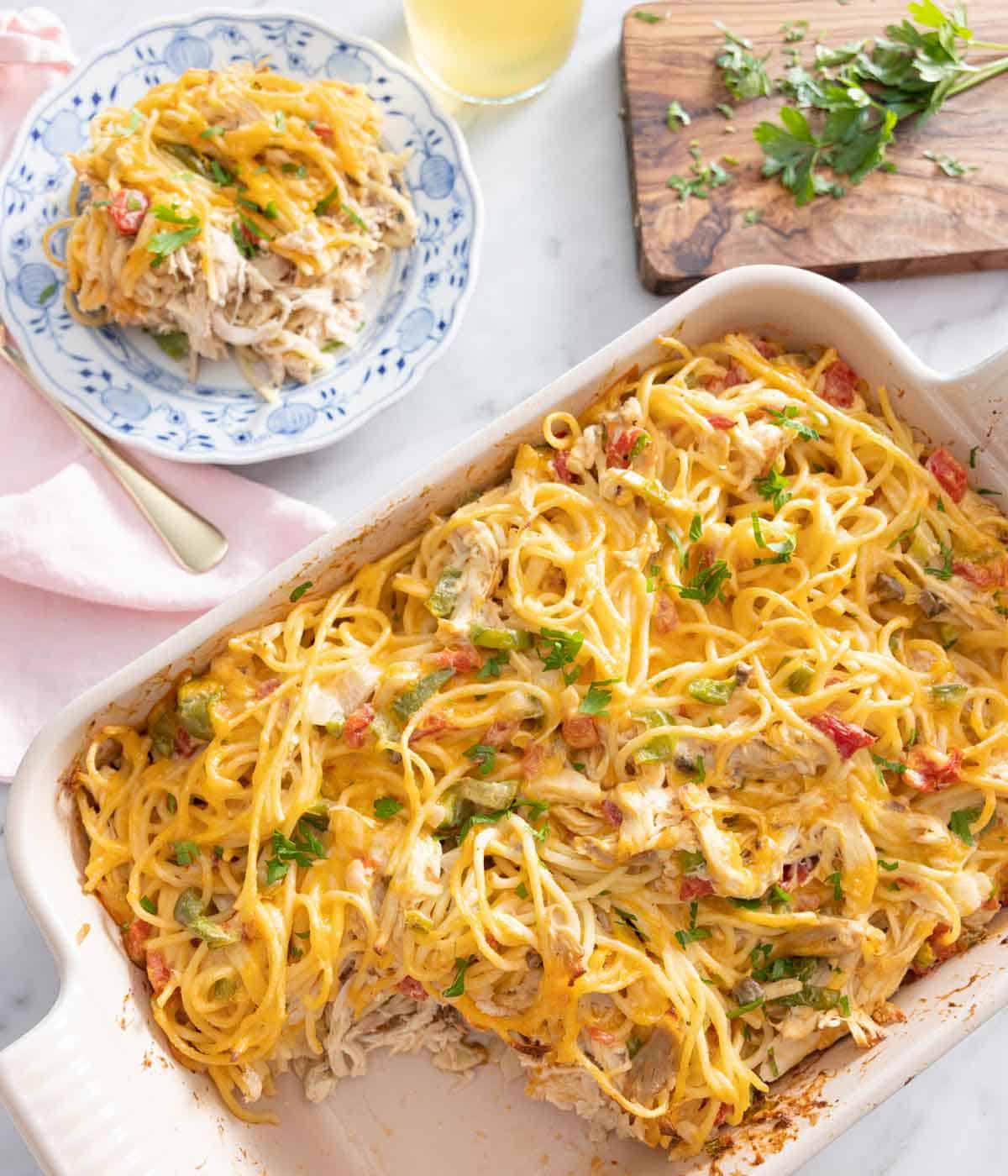 Overhead view of a casserole dish of chicken spaghetti with a plate beside it.