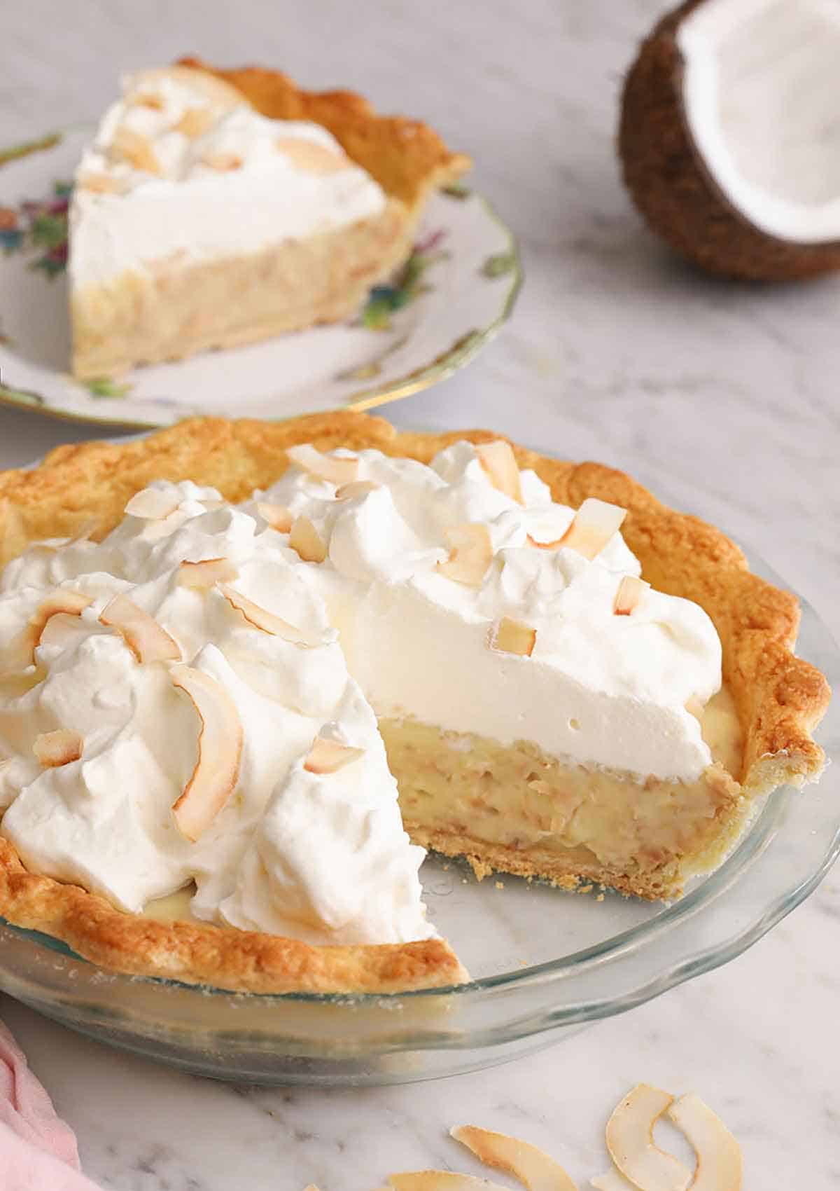A coconut cream pie in a glass pie dish with a slice cut out.